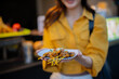 © Laingzaifa - An Asian woman is strolling through a night market, enjoying traditional street food, colorful lanterns, and smiling at the bustling city stalls. It's a vibrant atmosphere and a wonderful cultural