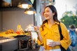 © Laingzaifa - An Asian woman is strolling through a night market, enjoying traditional street food, colorful lanterns, and smiling at the bustling city stalls. It's a vibrant atmosphere and a wonderful