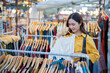 © Laingzaifa - An Asian woman is happily browsing for fashionable clothes in a boutique, smiling as she shops, holding shopping bags, showcasing the enjoyment of modern shopping.