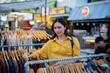 © Laingzaifa - An Asian woman is happily browsing for fashionable clothes in a boutique, smiling as she shops, holding shopping bags, showcasing the enjoyment of modern shopping.