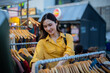 © Laingzaifa - An Asian woman is happily browsing for fashionable clothes in a boutique, smiling as she shops, holding shopping bags, showcasing the enjoyment of modern shopping.