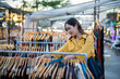 © Laingzaifa - An Asian woman is happily browsing for fashionable clothes in a boutique, smiling as she shops, holding shopping bags, showcasing the enjoyment of modern shopping.