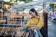 © Laingzaifa - An Asian woman is happily browsing for fashionable clothes in a boutique, smiling as she shops, holding shopping bags, showcasing the enjoyment of modern shopping.