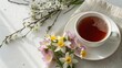 © adaptable_ Lark98A1 - A cup of tea on a beige napkin beside delicate spring flowers and blossoming branches on a white surface with soft natural light.