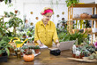 © sofiko14 - A woman in a yellow shirt works on a laptop surrounded by plants and succulents