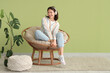 © Pixel-Shot - Young woman with headphones sitting in cocoon chair near green wall