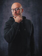 © mark_gusev - A man wearing a black hoodie and glasses is smiling. He is standing in front of a grey background. Classic portrait of a confident and friendly looking male model.