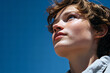 © EricMiguel - Thoughtful young student with short curly hair, blue eyes and freckles gazing upward in a light - gray hoodie against a vivid clear blue sky