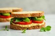 © Prakaikan - A delectable vegetarian sandwich featuring hummus, ripe tomato slices, and crisp cucumber, nestled between slices of artisan bread and garnished with fresh basil leaves.