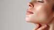 © Olga Ко - Close up side vtouchiofile of beautiful young woman with perfect glowing glass skin touching her neck. Mockup for skincare advertisement with copy space on grey background.