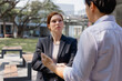© Tj - Business executive woman listening intently to her male colleague talking during an informal discussion outdoors, representing teamwork and professional communication in a modern work environment