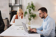 © Stockphotodirectors - Two team members collaborate in a modern office. One person types on a laptop while another works on a separate device. They focus on tasks at hand and share ideas.
