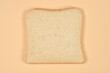 © nahhan - A single square slice of fresh white sandwich bread is centered on a plain light beige background shot from a top down perspective.