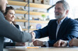 © opolja - Happy businessmen shaking hands at group board meeting