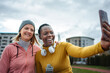 © Jelena - Diverse women friends smiling taking selfie outdoors after workout