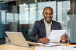© Liubomir - Senior businessman smiling, viewing documents and working on a laptop at a modern corporate office, representing success, leadership, and professional achievement in business