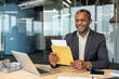 © Liubomir - Mature professional man smiling at his desk as he opens an important envelope to reveal documents and good news on his laptop in a modern office, pleased and confident