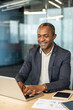 © Liubomir - Successful african american businessman smiling and typing on a laptop, managing tasks and communicating effectively while sitting at a desk in a contemporary corporate environment
