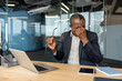© Liubomir - Mature african american businessman at his desk rubbing his eyes and holding glasses, suffering headache and eye strain from long laptop use, showing work fatigue and stress