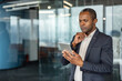 © Liubomir - Mature businessman standing, looking concentrated at a digital tablet while thinking and strategizing in a contemporary office environment, reflecting business analysis and innovation