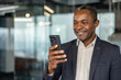 © Liubomir - Happy mature man smiling while holding and looking at a cell phone, communicating and connecting with digital technology in a professional modern office environment