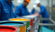 © Rhony - Close-up of colorful paint cans on a production line, with workers working in the background.