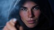 © Thares2020 - A mysterious hooded figure makes direct eye contact and points forward with a determined expression in a smoky high contrast portrait