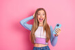 © deagreez - Young woman with a cheerful expression holding a smartphone against a vibrant pink background, conveying joy and excitement