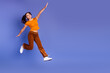 © deagreez - Young female teen jumps in a vibrant orange top and brown pants against a purple studio background for fashion lifestyle and fitness concept