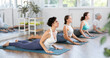 © JackF - Group of women bending in back while lying on stomach in Bhujangasana Cobra Stretch position during training together in yoga studio
