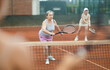 © JackF - Emotional aged woman enthusiastically playing tennis outdoors in summer, swinging racket to hit ball during doubles match with female partner in background on court..