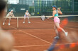 © JackF - Emotional fit young girl, seen from behind, enthusiastically playing tennis outdoors, performing left-handed forehand to return ball to opponent court during doubles match with female partner..