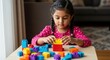 © Steven - Little girl building and stacking colorful blocks on table with focused concentration in a cozy indoor setting quietly.