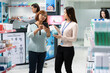 © DC Studio - Female pharmacy employee consults with customer using mobile reference, discussing prescription details and suitable health supplements with middle aged client in modern drugstore.