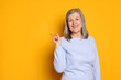 © New Africa - Beautiful senior woman pointing at something on yellow background. Space for text