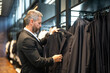 © Volodymyr - Business man in a suit in a suit boutique. A businessman confidently chooses elegant suit in store. A trendy customer examines jacket while shopping formal suit. A charming model in classic outfit.