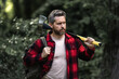 © Volodymyr - Lumberjack in plaid shirt with jeans carry large axe in summer wood. Manual Work. Natural environment. Lumberjack with an axe in forest. Hard working man. Brutal bearded man with an axe or hatchet.