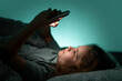 © Volodymyr - Teenager chatting on phone in bed at night. Child texting on phone in bed at night. Kid scrolling phone under blanket at night. Teenager browsing internet on phone in bed at night.
