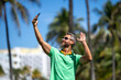 © Volodymyr - Tourist man takes a selfie near palm tree. Man captures a selfie during summer vacation. Traveler snaps a selfie in a tropical destination. A selfie with palm trees captures the tropical vibes.