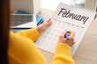 © Pixel-Shot - Woman marking day on flip calendar at table, closeup
