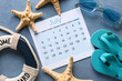 © Pixel-Shot - Calendar with flip flops, sunglasses and beach decor on blue grunge background. Summer vacation concept
