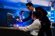 © ultramansk - Professional male software engineer pointing at computer screen to help female programmer. IT development team working on coding data analysis in dark cyber security workplace.
