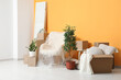 © Pixel-Shot - Interior of new living room with packed armchair, houseplants and cardboard boxes. Moving house concept