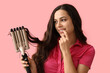 © Pixel-Shot - Beautiful young woman with curling iron on pink background