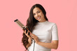© Pixel-Shot - Beautiful young woman with curling iron on pink background