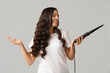 © Pixel-Shot - Beautiful young woman with curling iron on grey background
