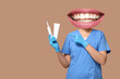 © Pixel-Shot - Young female dentist pointing at electric toothbrush and toothpaste on beige background
