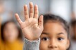 © whitestorm - A close-up shot of a young, vibrant student raising her hand in class, with other students visible in the blurred background, showcasing an engaging and educational environment.