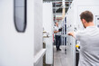 © Westend61 - Two men talking at machinery in factory shop floor