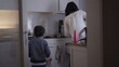 © Marco - Young boy walking into kitchen holding craft project, mother holding baby near kitchen counter, everyday family interaction during household routine
